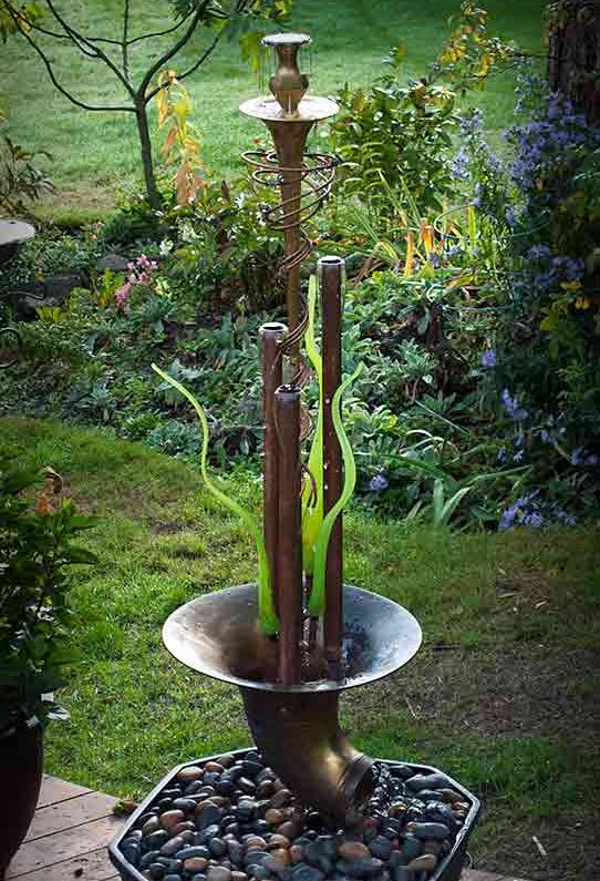 This fountain comprises three large copper tubes and three hand blown glass reeds centered in a tuba bell.  Water flows up and over the copper tubes forming water bells. It comes complete with water reservoir and pump and is currently available for purchase @ $ 2,400. Please call or email for further info and shipping details.